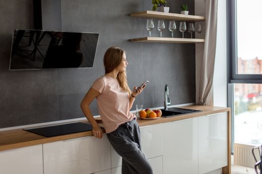 nainen seisoo keittiössä puhelin kädessä